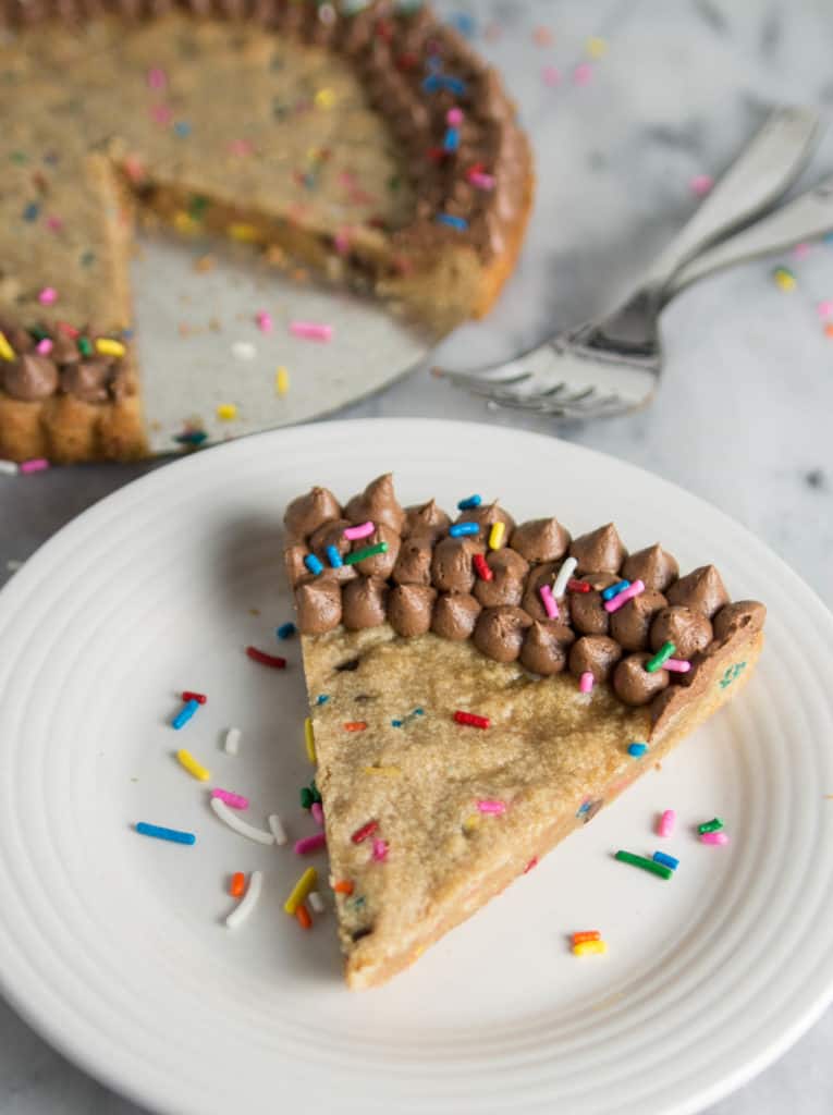 overhead shot of a slice of funfetti peanut butter cookie cake on a plate with the rest of the cookie cake in the background