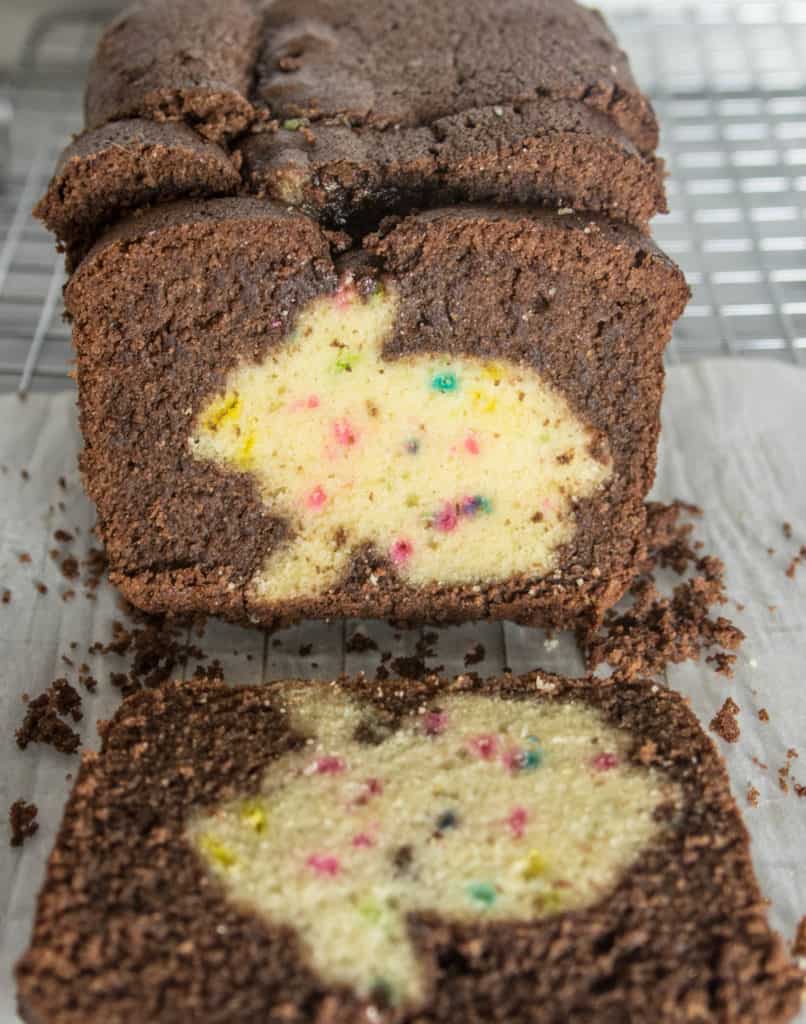 slices of chocolate funfetti hidden bunny cake sitting on a piece of parchment on top of a wire rack