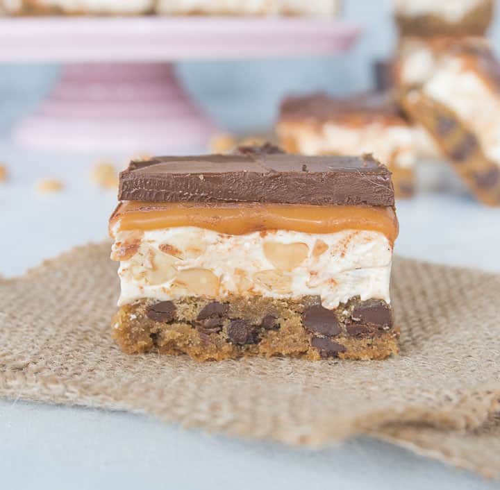 cookie bar sitting on a piece of burlap with more chocolate chip cookie snickers bars in the background