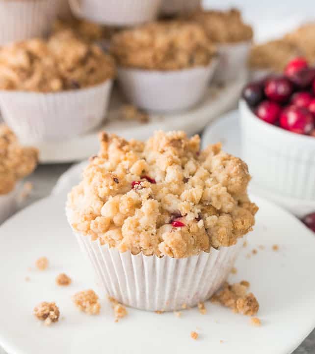 muffin on a plate with cranberries and more white chocolate cranberry crumb muffins in the background