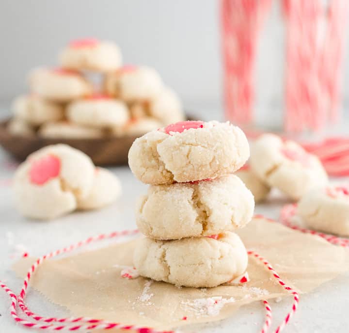 stack of white chocolate peppermint thumbprint cookies with more cookies and candy canes in the background