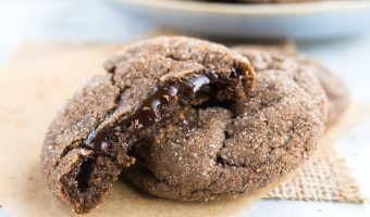 three cookies with one torn in half to reveal the molten chocolate center and a bowl of more cookies in the background