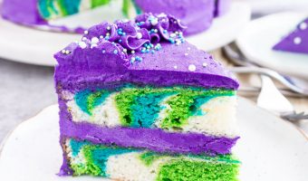 image of a slice of mermaid layer cake sitting on a plate with the rest of the cake in the background