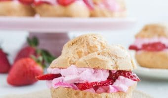 strawberry cream puff sitting on a piece of burlap with a cake stand topped with cream puffs in the background
