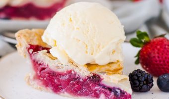 slice of bumbleberry pie on a plate with a scoop of ice cream on top and berries next to it