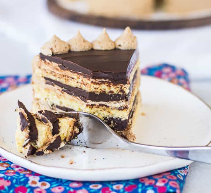 slice of opera cake on a plate with a fork taking a bite out of it