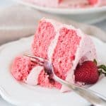 slice of strawberry layer cake on a plate with a fork taking a bite out of it