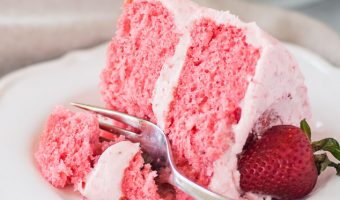 slice of strawberry layer cake on a plate with a fork taking a bite out of it