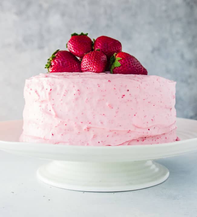 whole strawberry layer cake on a cake stand and topped with strawberries