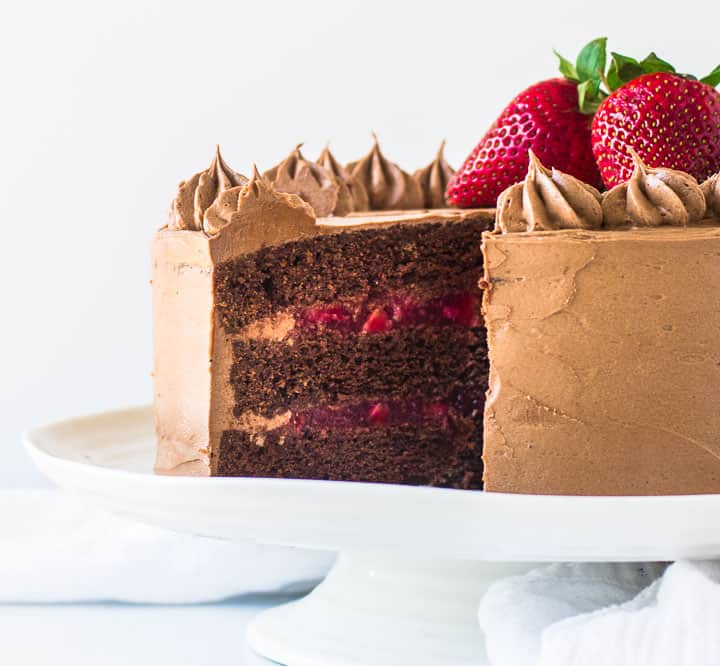 chocolate strawberry cake on a cake stand with a slice taken out of it