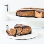 slice of triple chocolate cheesecake on a plate with the rest of the cake in the background