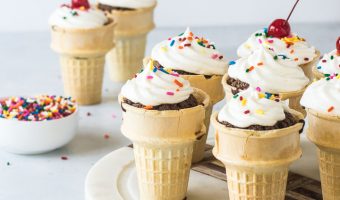ice cream cone cupcakes on a cake stand with a dish of sprinkles and more cupcakes behind it