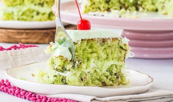 slice of Watergate cake with a cherry on top and a fork taking a bite out of the cake