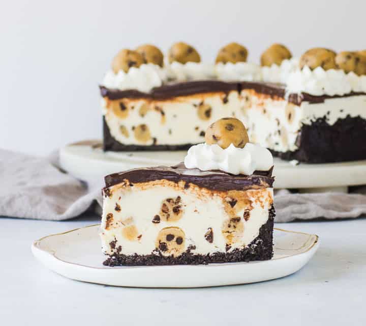 slice of cookie dough cheesecake on a plate with the rest of the cake in the background