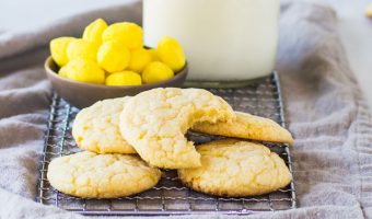 lemon drop cookies on a wire rack in front of a dish of lemon drops and a bottle of milk