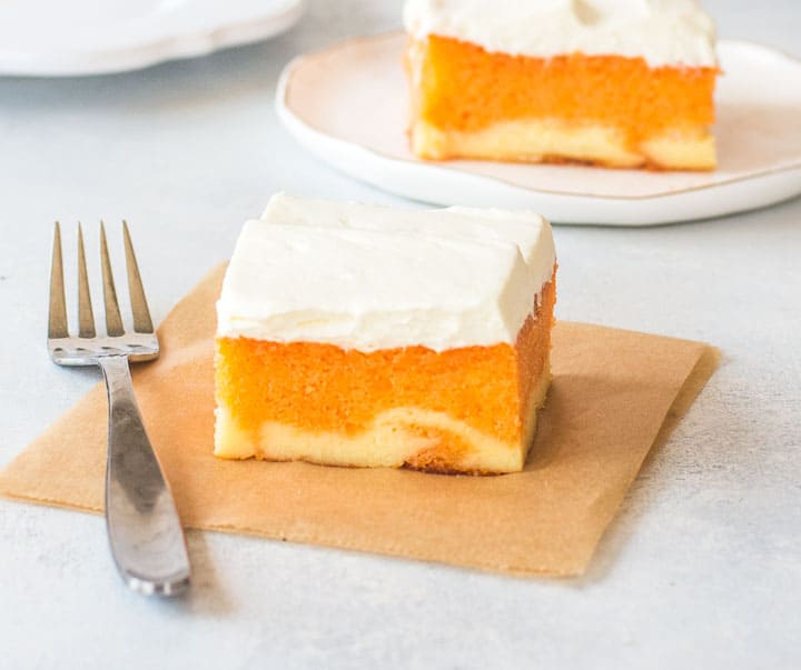 slice of orange creamsicle cake on a piece of parchment with another slice of cake behind it