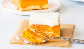 slice of orange creamsicle cake on a piece of parchment with a fork taking a bite out of it