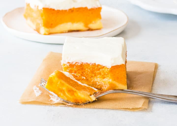 slice of orange creamsicle cake on a piece of parchment with a fork taking a bite out of it