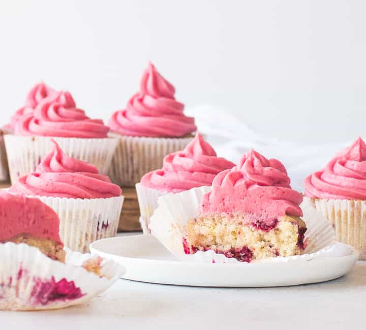 raspberry cupcake cut in half sitting on a plate with more cupcakes behind it