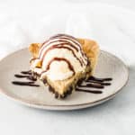 slice of chocolate chip pie on a plate topped with ice cream and chocolate sauce