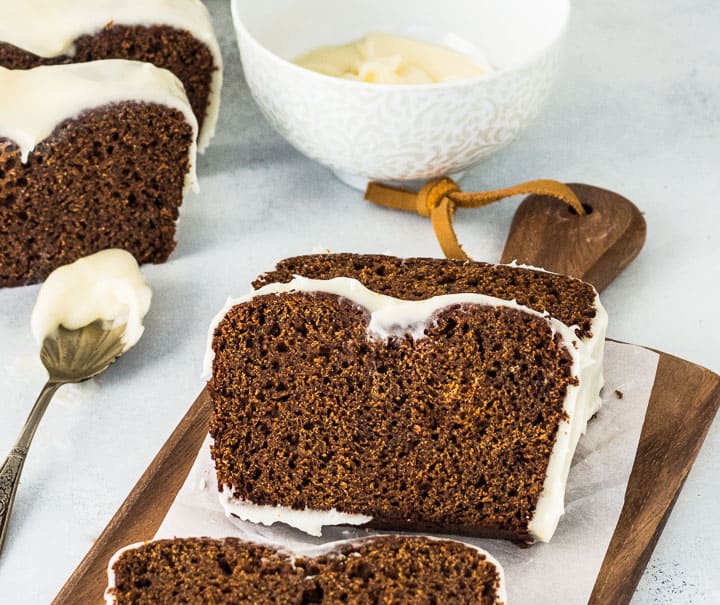 sliced gingerbread loaf on a wooden cutting board with a bowl of glaze behind it