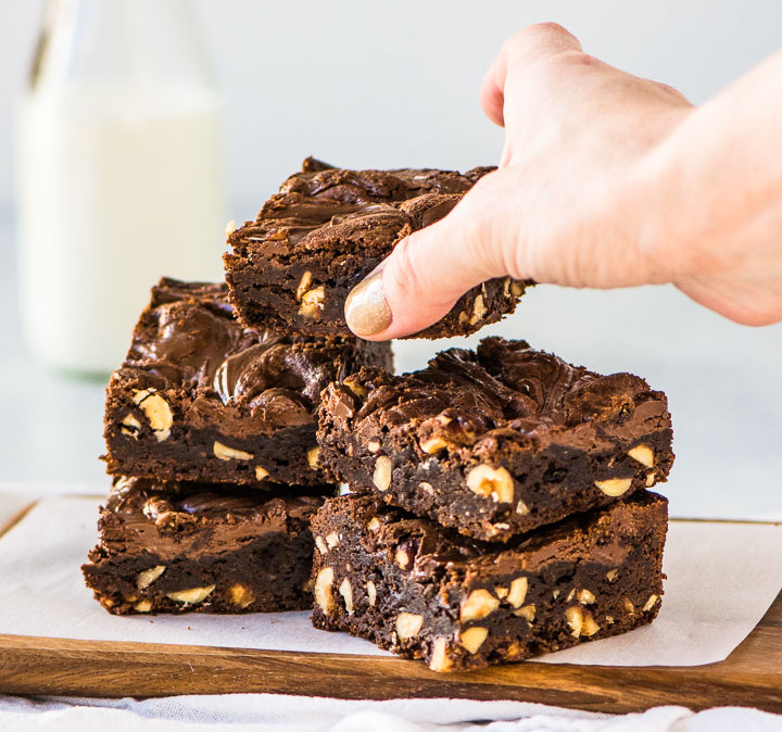 hand reaching for a chocolate hazelnut brownie that's on top of a stack of brownies