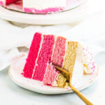 slice of pink ombre cake on a plate with a fork taking a bite out of it