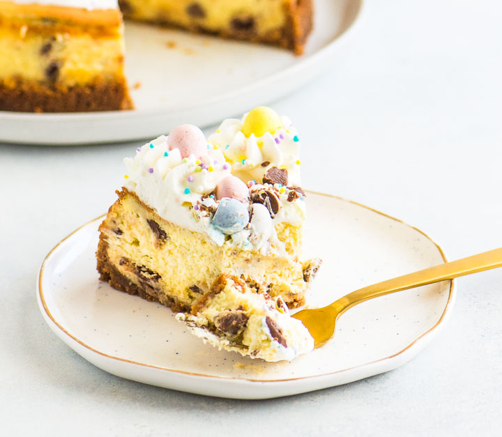 slice of Easter egg cheesecake on a plate with a fork taking a bite out of it and the rest of the cake in the background