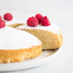 sliced cake on a cake plate with powdered sugar and raspberries on top