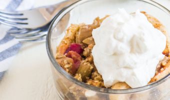 crisp in a bowl with whipped cream on top and two forks and a dish towel behind it