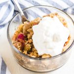scoop of apple rhubarb crisp in a bowl with a striped towel behind it