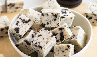 bowl of fudge with Oreos stacked behind it and white chocolate chips scattered in front of it