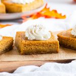 three pumpkin pie bars on a serving board in front of a plate of more bars