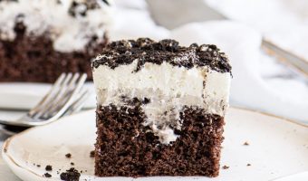 slice of Oreo poke cake on a plate with a fork and another cake slice in the background