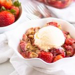 bowl of strawberry crumble topped with ice cream with a bowl of fresh strawberries in the background