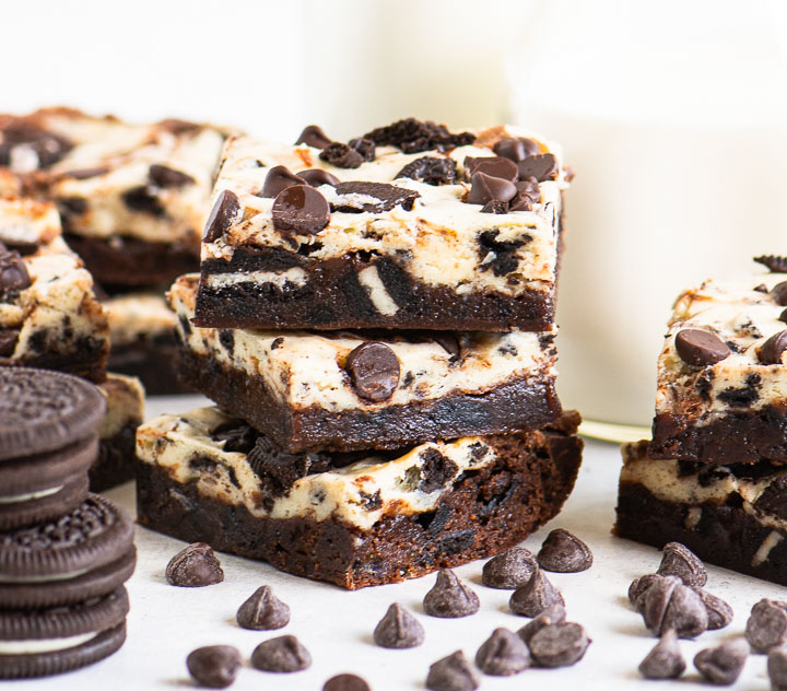 three brownies stacked in front of a glass milk bottle with chocolate chips in front