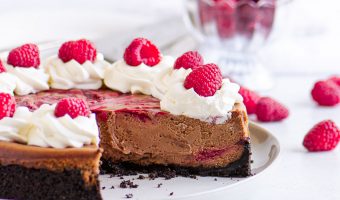 sliced cheesecake on a cake plate in front of a dish of raspberries