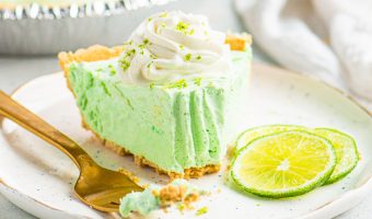 slice of pie topped with whipped cream in between a gold fork and lime slices