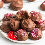 chocolate covered cherry cookies stacked on a plate with more cookies in the background