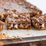 Nutella magic bars cut into squares on parchment paper showing layers of graham crust, gooey Nutella filling, coconut, baking chips, and chopped nuts.