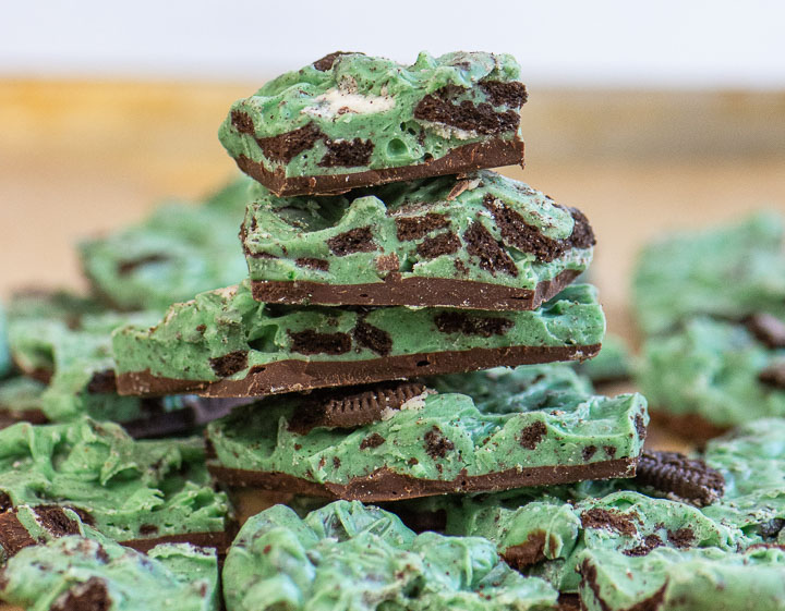 Close-up stack of green peppermint Oreo bark showing the chocolate base and crushed Oreo pieces, with more bark scattered on the baking sheet behind it.