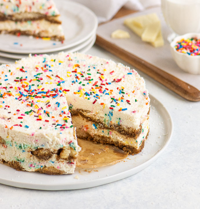 sliced birthday cake tiramisu on a white cake plate with stack of plates in the backgroud